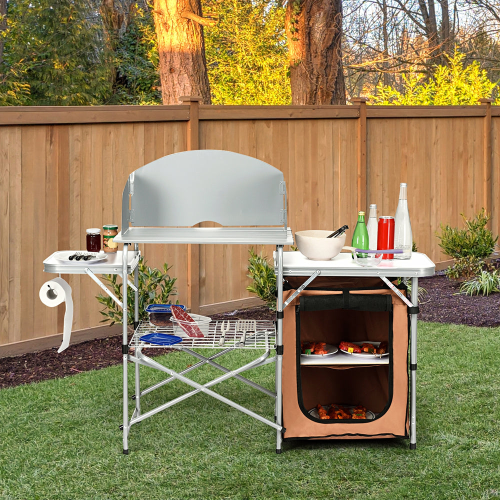 Foldable outdoor BBQ grilling table with windscreen, featuring aluminum frame, side tables, and zippered storage bag.