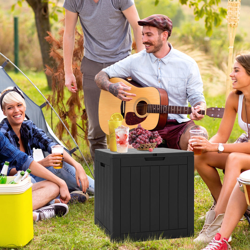 Black 30-gallon deck box with woodgrain surface, used as a side table during outdoor gathering.