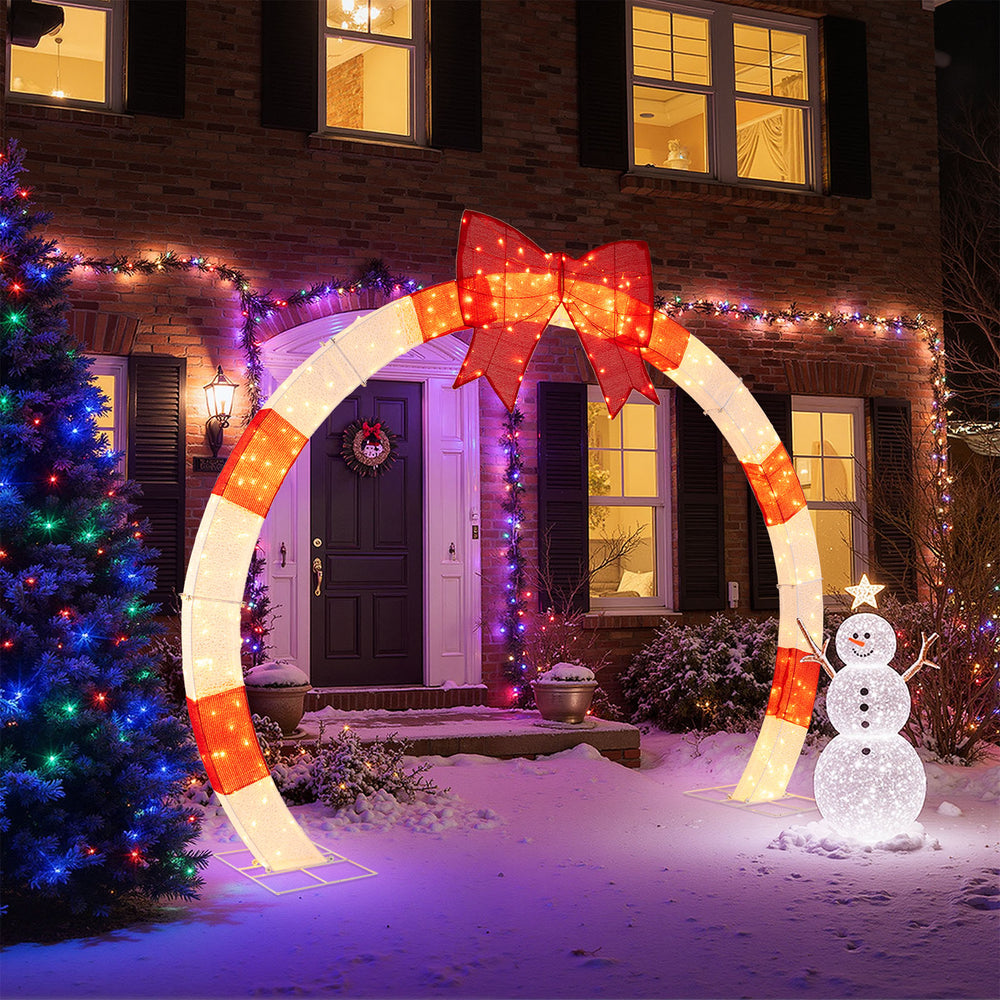 Christmas archway with large bow and warm white LED lights, perfect for yards and porches during the holiday season.