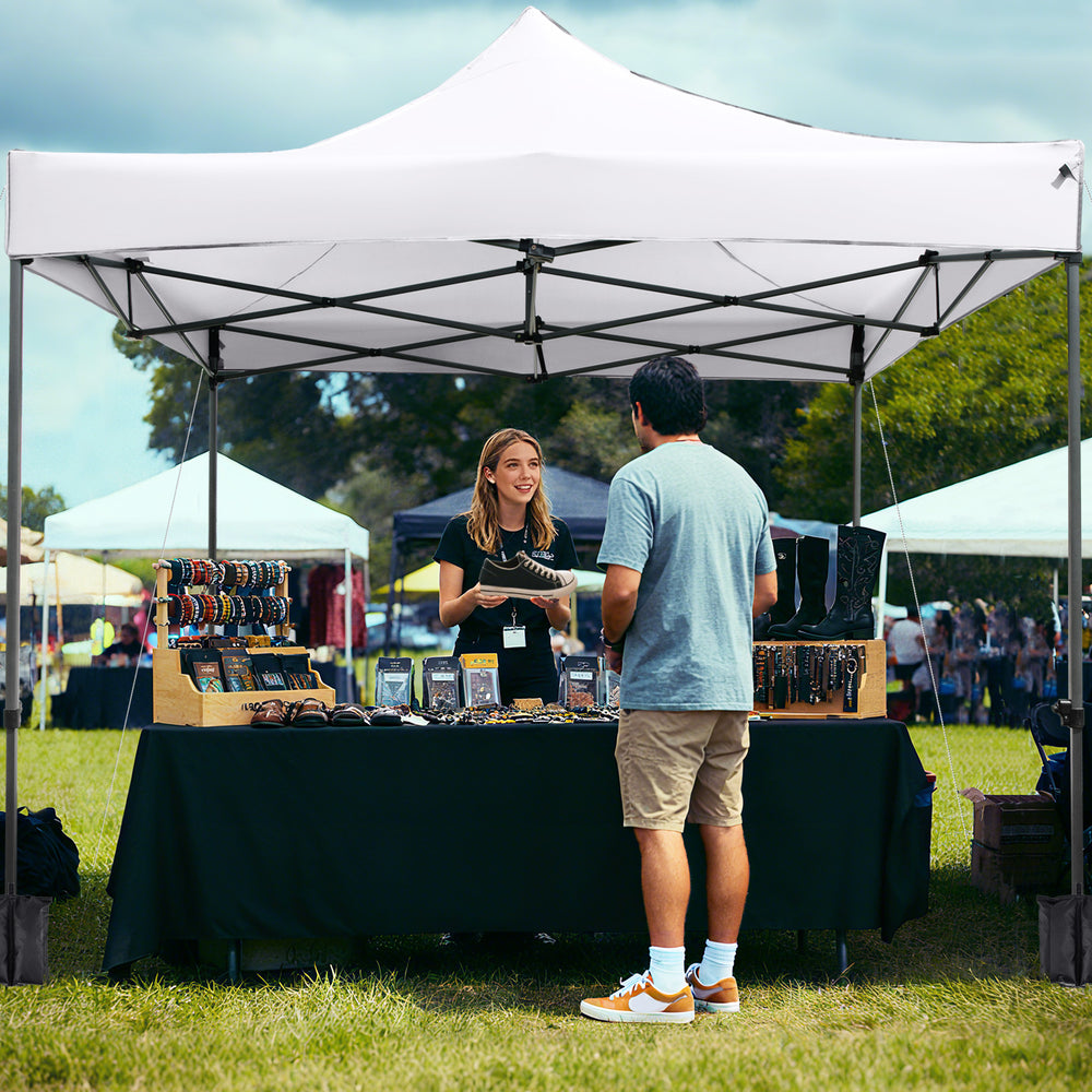 White 10 x 10 FT outdoor pop-up canopy tent set up at a market, featuring a sturdy metal frame and water-resistant.
