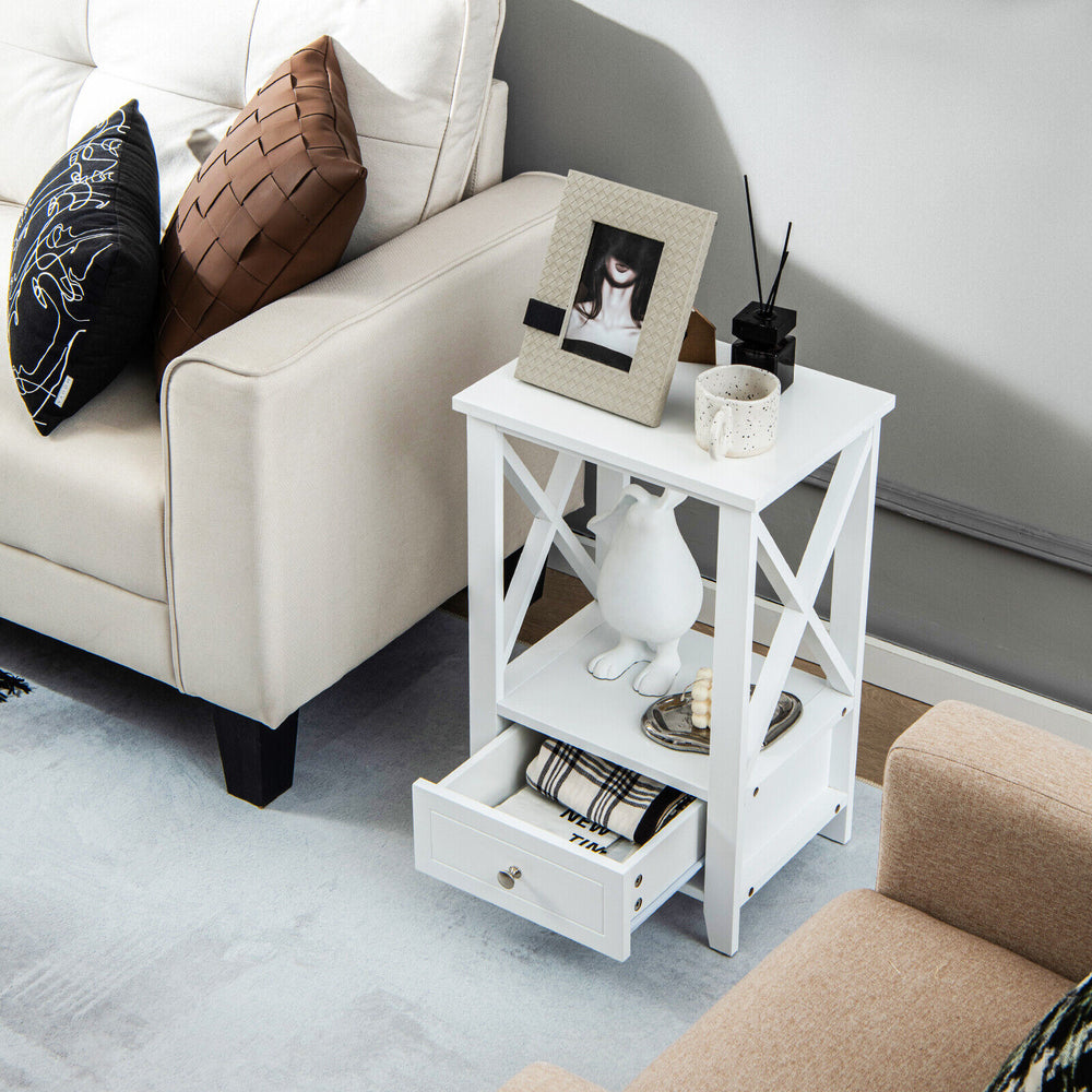 White 2-tier nightstand with storage drawer, open shelf, and X-shaped structure for versatile use beside a sofa.