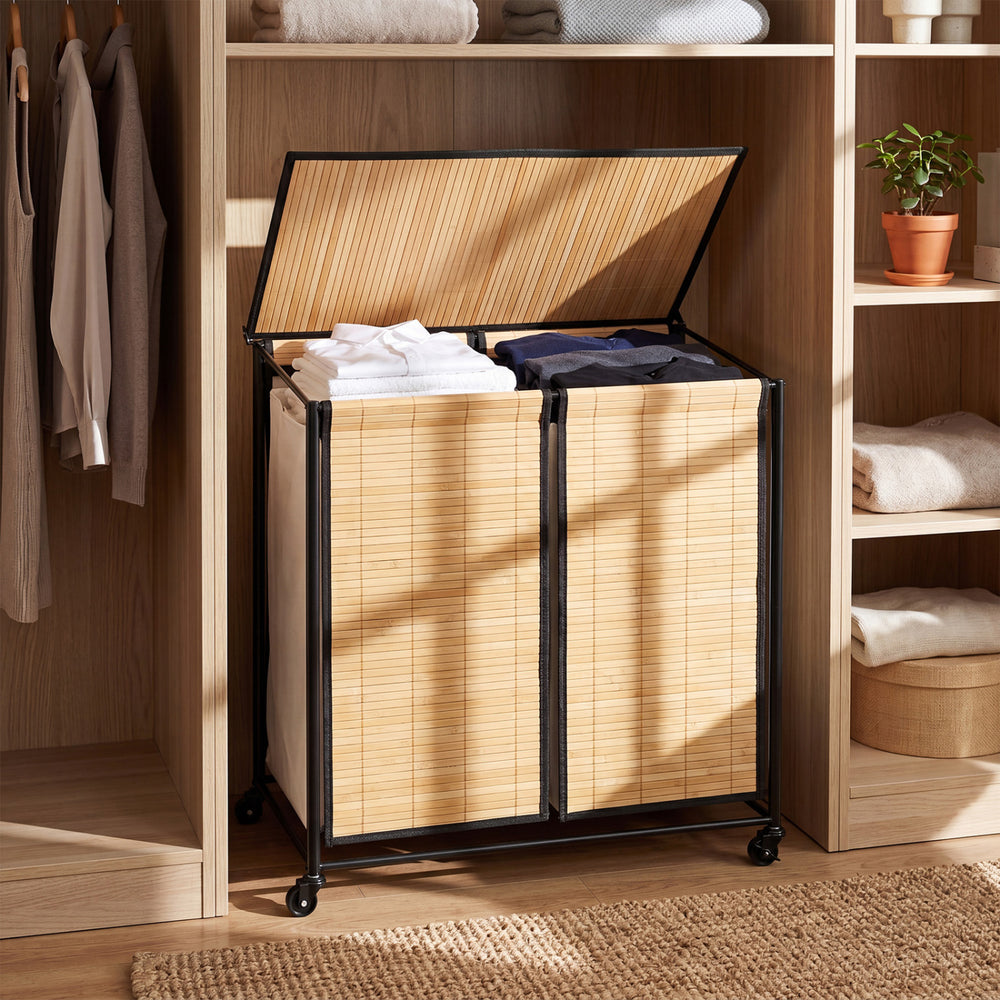 Two-section natural bamboo laundry hamper with lid and lockable wheels for easy sorting and secure placement.