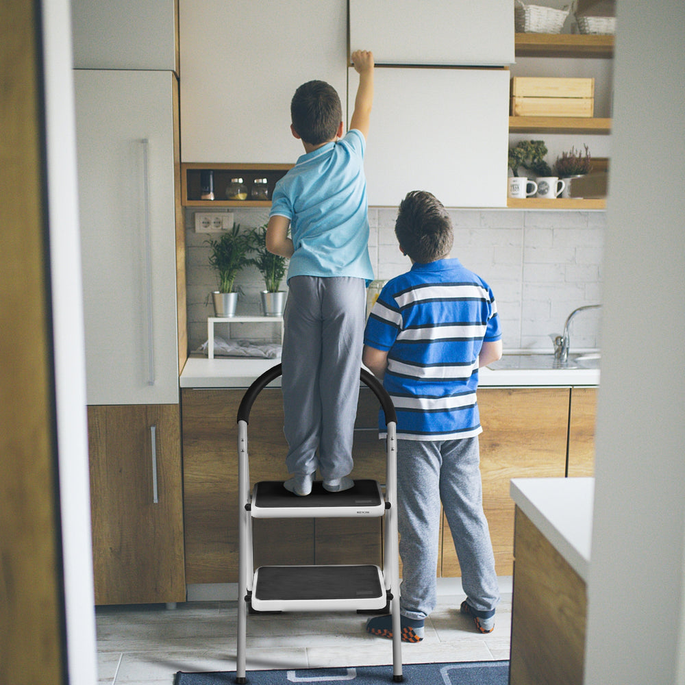 Two children using a 2.75 feet folding step stool with anti-slip pedals in a modern kitchen for reaching high cabinets.