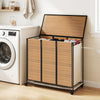 Three-section laundry hamper with lid and natural bamboo slats, designed for sorting clothes in small spaces.