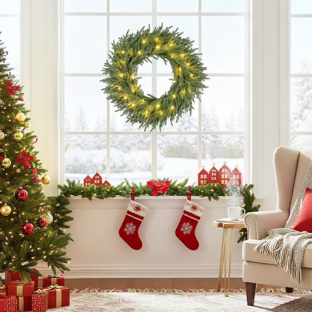 24-inch pre-lit Christmas wreath with 35 warm white LED lights, displayed on a window for festive holiday decor.
