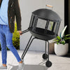 28-inch portable black fire pit on wheels with log grate, ideal for heating or barbecue, shown being moved outdoors.