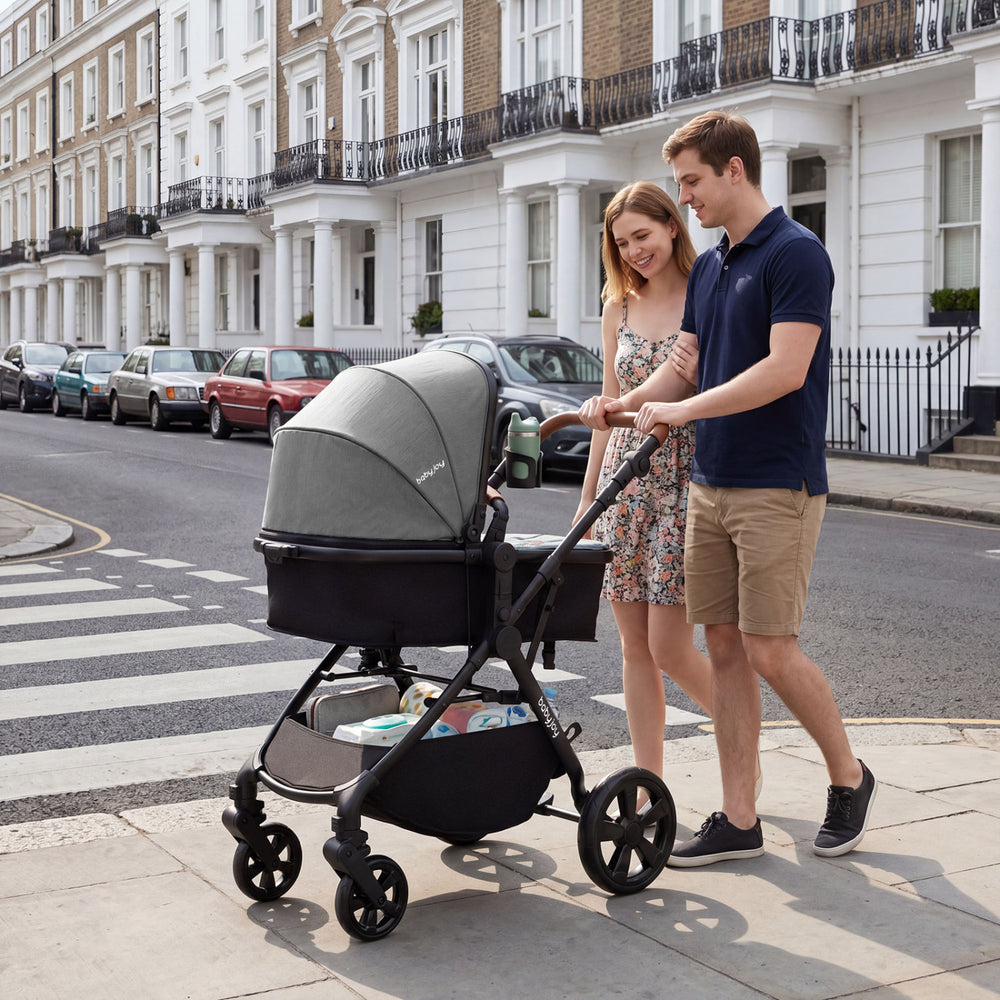 Convertible gray baby stroller with car seat adapters, shown in use on a city street by a couple.