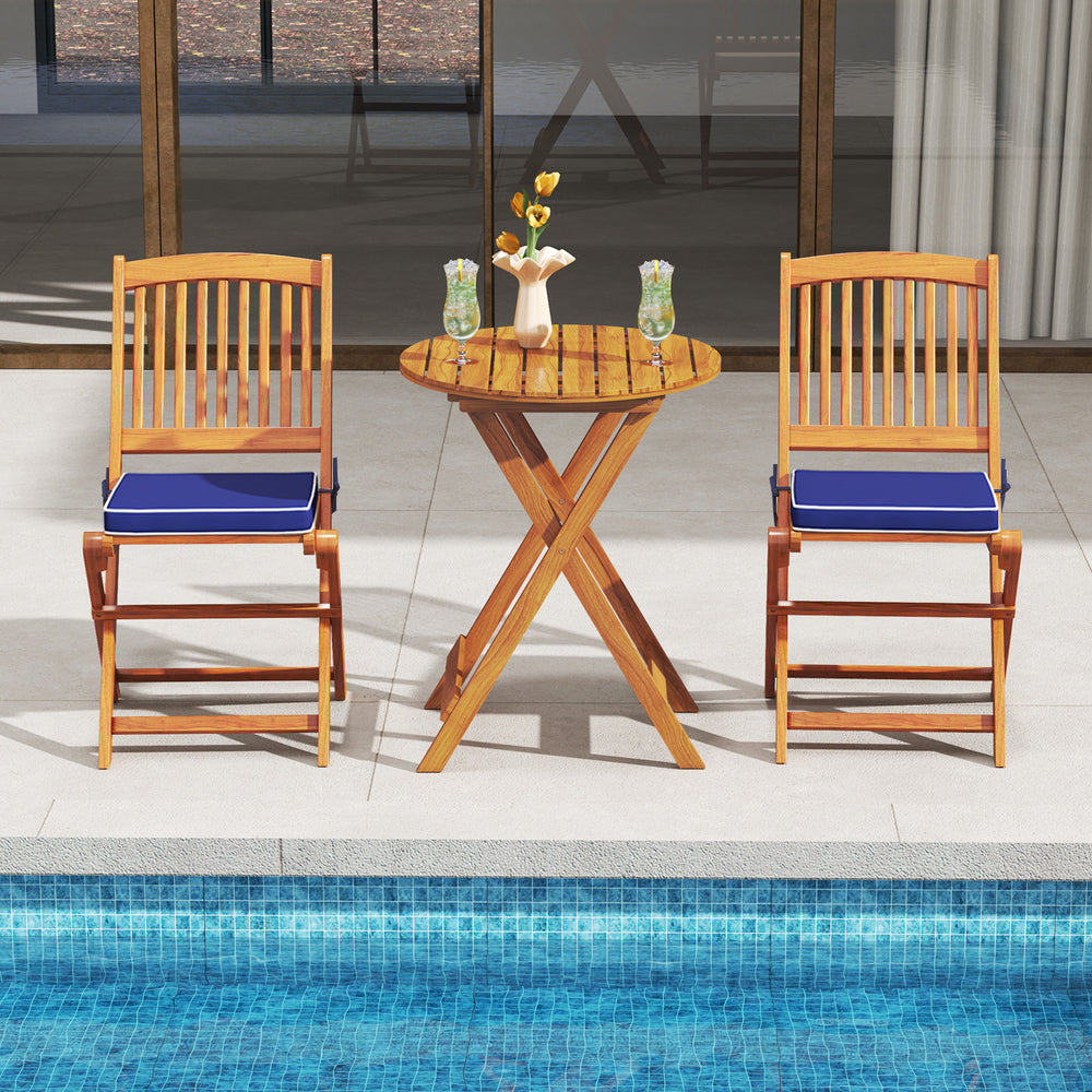 Two outdoor folding chairs with navy seat cushions and a wooden table, perfect for poolside dining or relaxation.