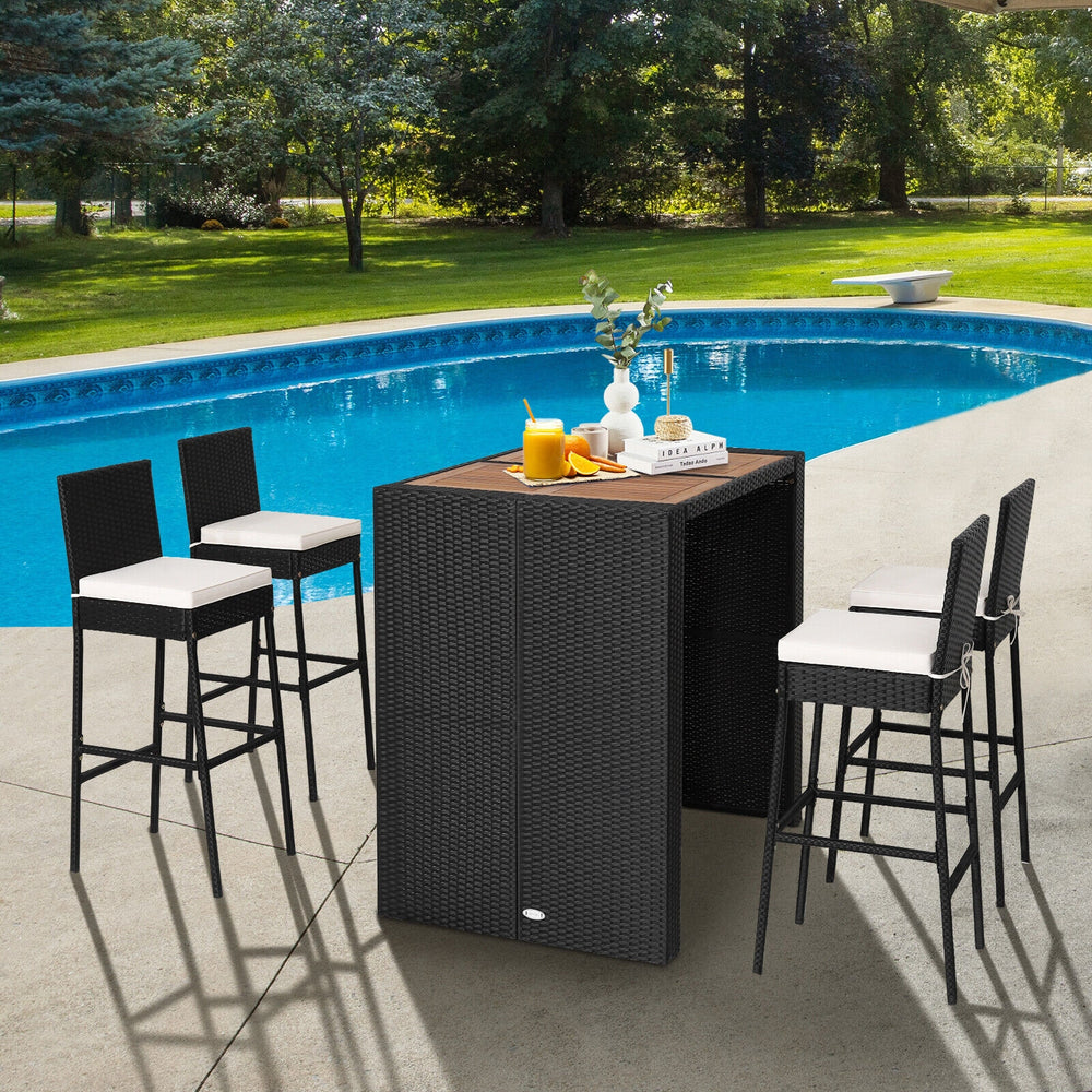 5-piece patio dining set featuring a solid acacia wood tabletop and black PE wicker bar stools with cushions by the.