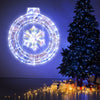 33-inch lighted snowflake wreath with 128 LED lights, displayed on a wall beside a Christmas tree and wrapped gifts.