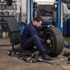 Mechanic using a 36" 3-in-1 folding creeper with padded seat for comfort while changing a tire in a garage.