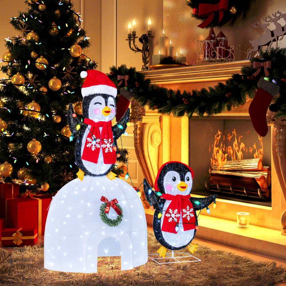 3D pre-lit igloo with two penguins in scarves, decorated with a wreath and 170 cold-white LED lights for festive decor.