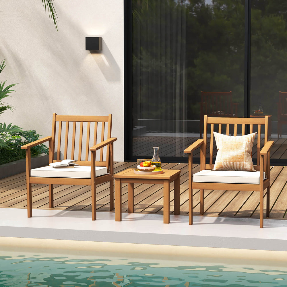 Two acacia wood chairs with soft cushions and a matching table, perfect for backyard or poolside relaxation.