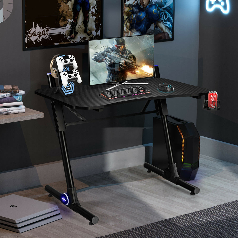 Gaming desk featuring a carbon fiber textured surface, cup holder, and blue LED lights for an enhanced gaming.