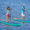 Two people paddle on 10 feet inflatable stand-up paddle boards in a lake, ideal for water activities and stability.
