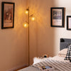 Three-globe floor lamp in gold with acrylic shades, foot switch, and a stable base, perfect for home or cafe lighting.