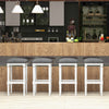 Set of two gray padded saddle stools with footrests, featuring a solid rubber wood frame for versatile bar or kitchen.