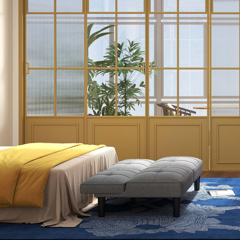 Convertible futon sofa bed in gray with padded seat, paired with a bedside table and accent chair for versatile bedroom.