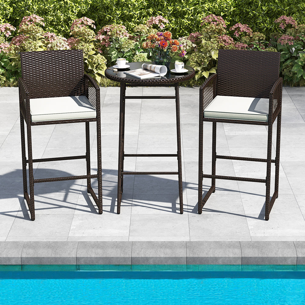 Bar height table and two armchairs in dark wicker with white cushions, perfect for poolside relaxation.