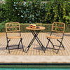 Folding round table and two chairs with handwoven rattan seats, perfect for outdoor patio and poolside relaxation.