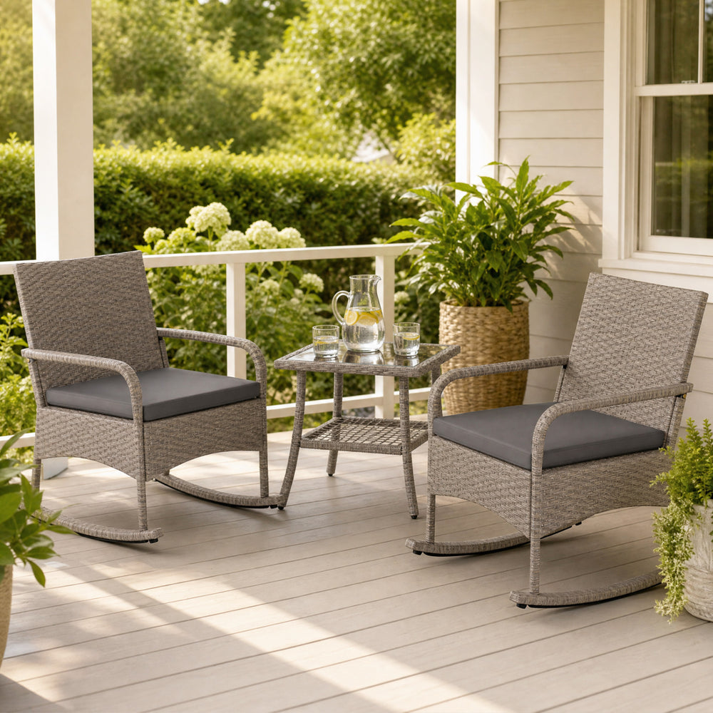 Two gray wicker rocking chairs with cushions and a coffee table, perfect for relaxing in the garden or backyard.