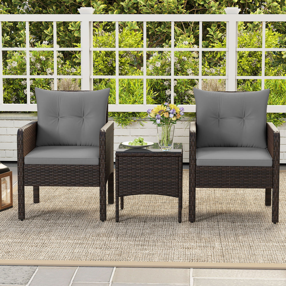 Two gray cushioned chairs with a square glass-top table in a patio setting, made of hand-woven PE rattan.