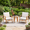 Two acacia wood chairs with off-white cushions and a side table create a cozy outdoor seating area for relaxation.