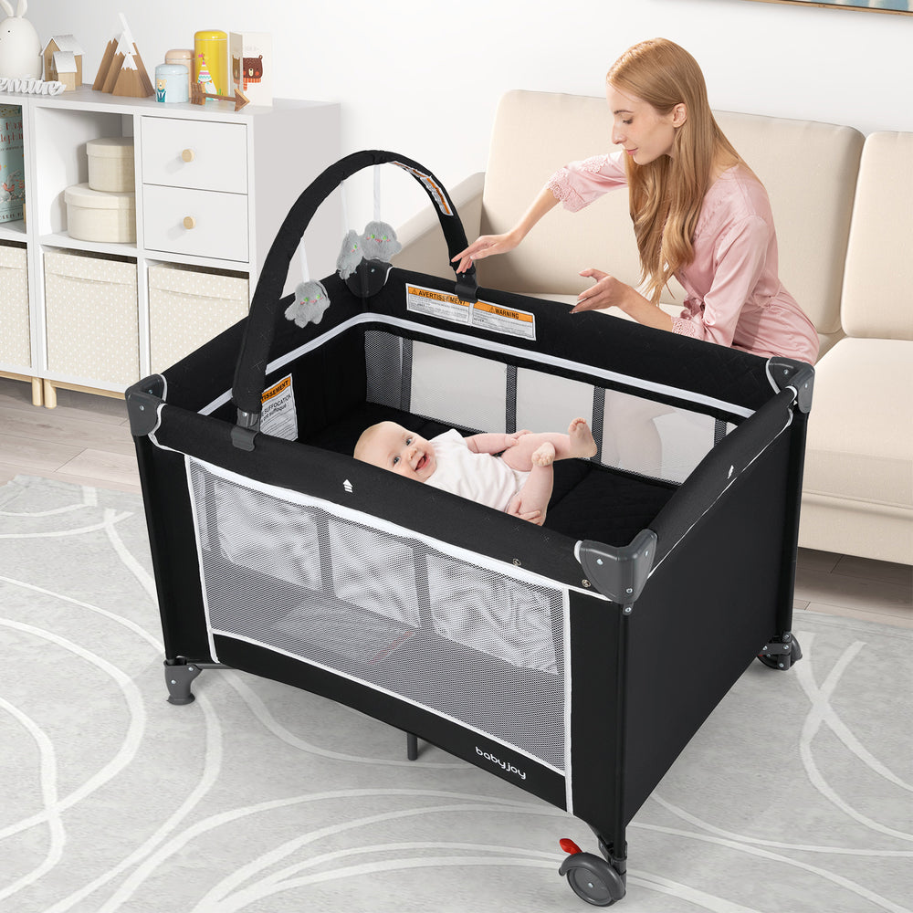 Portable baby crib and playpen in black with changing table, breathable mesh walls, and detachable toy bar for safety.