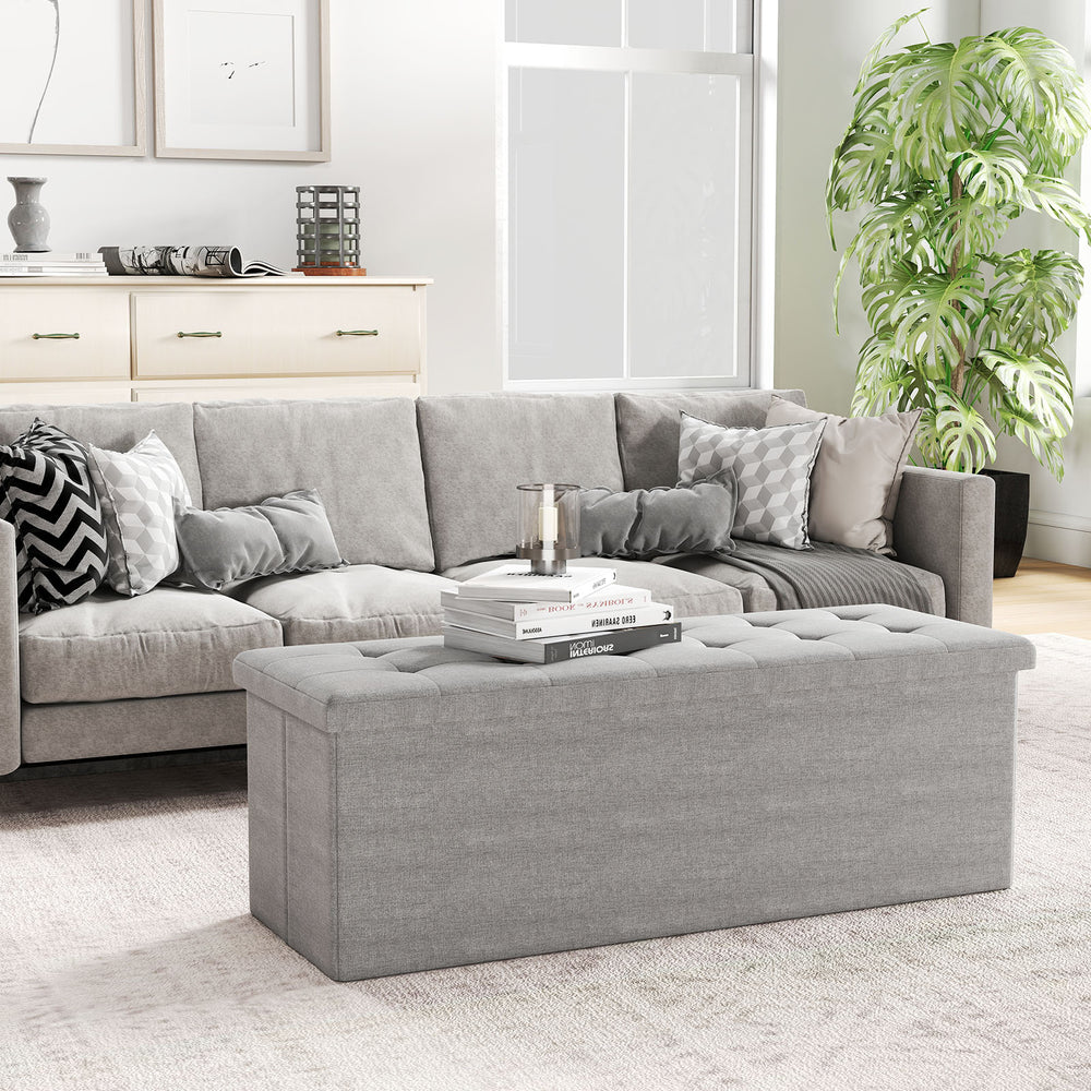 Light gray folding storage ottoman bench with padded seat, 38-gallon capacity, perfect for living room or bedroom use.