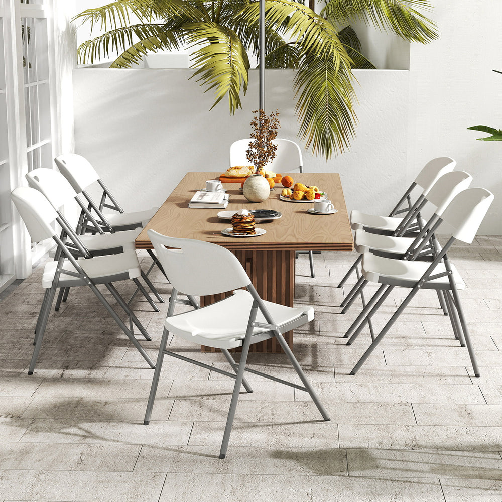 Eight white folding stackable chairs with metal frames around a wooden table, ideal for outdoor gatherings and events.