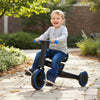 Toddler riding the navy 4-in-1 foldable tricycle with adjustable seat and parent steering handle on a pathway.