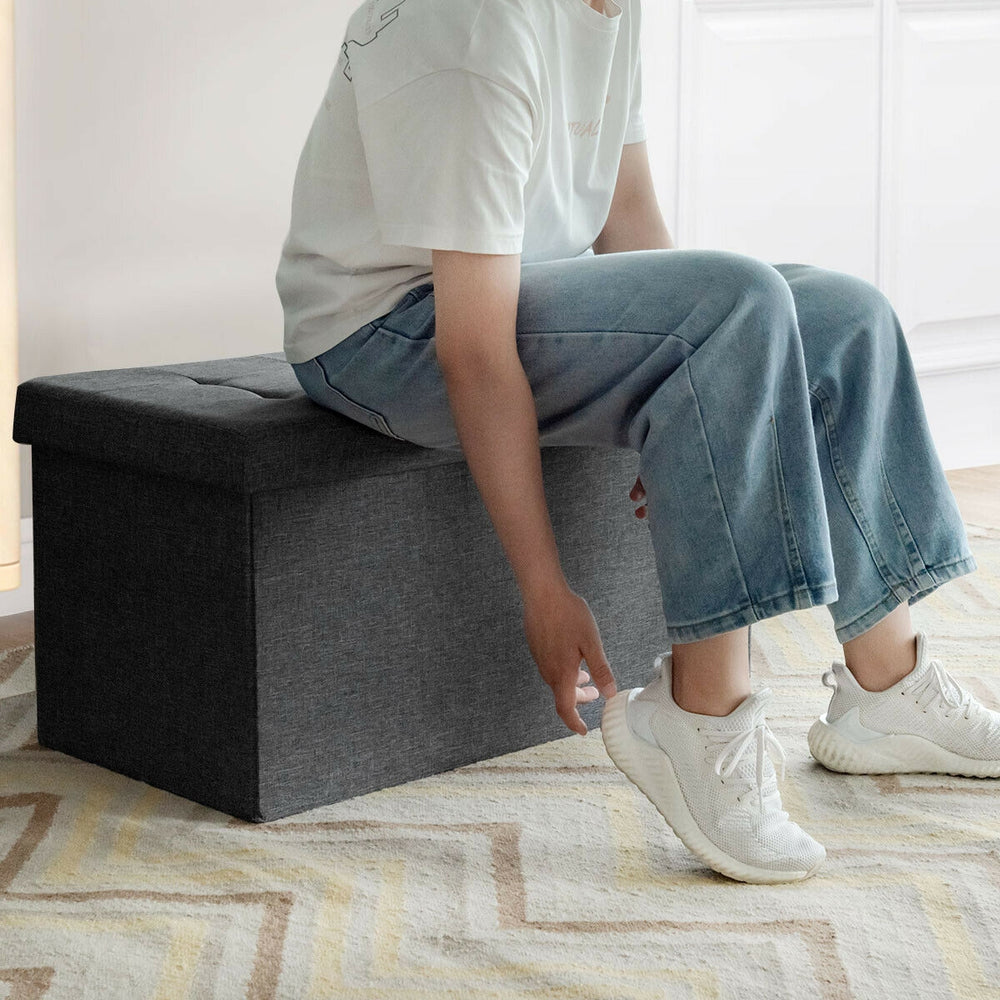 Foldable dark gray storage ottoman with removable bin, featuring a padded seat and spacious interior for versatile.