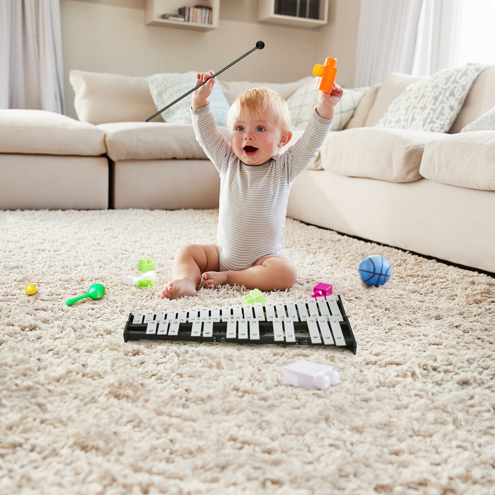 Child playing with a 32-note glockenspiel xylophone on a carpet, surrounded by colorful toys in a cozy living room.