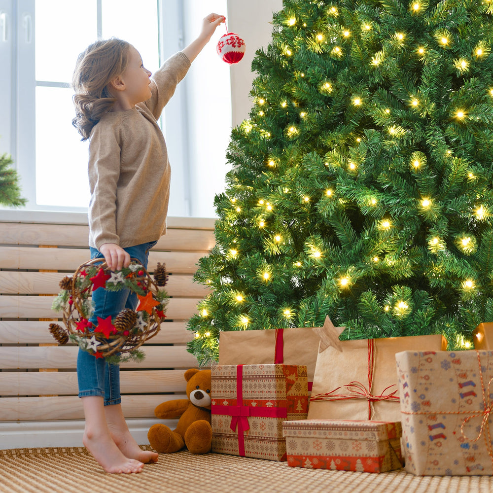 Child decorating a 7 ft PVC artificial Christmas tree with LED lights, surrounded by wrapped gifts for festive cheer.