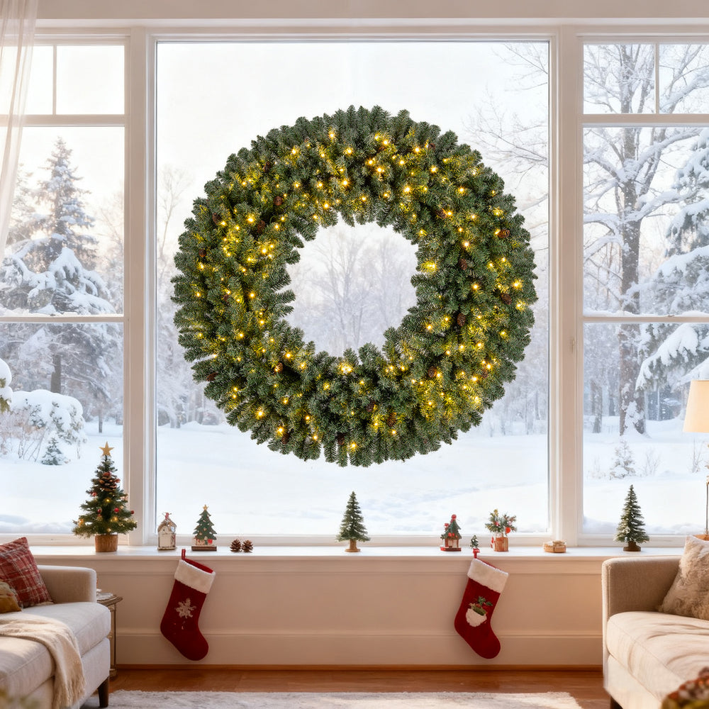 60-inch pre-lit artificial Christmas wreath with 200 warm white LED lights, displayed in a snowy window setting.