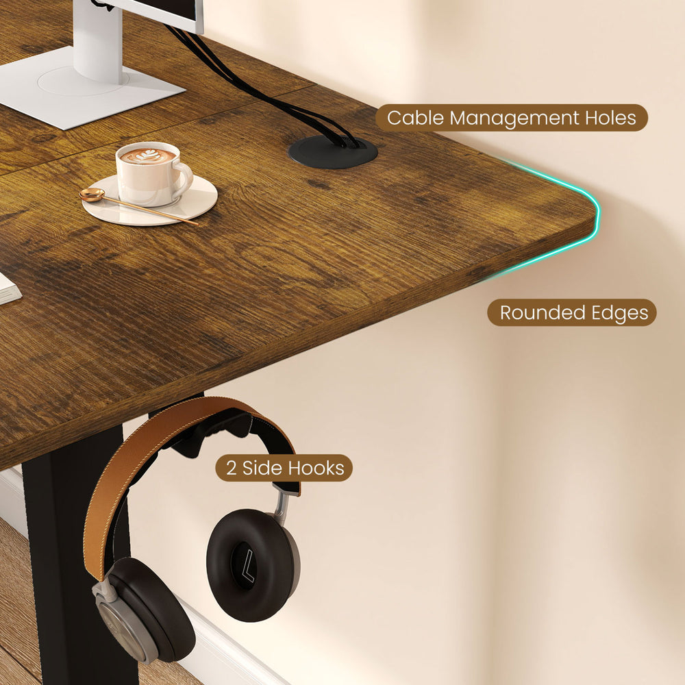 Close-up of the height adjustable desk showing cable management holes, rounded edges, and side hooks for headphones.