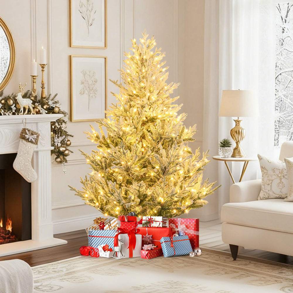 Hinged 6-foot pre-lit artificial Christmas tree with 340 warm white LED lights, set up near a cozy fireplace and gifts.