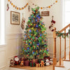 Pre-lit artificial Christmas tree with pine cones, red berries, and multicolor LED lights decorates an indoor holiday scene.