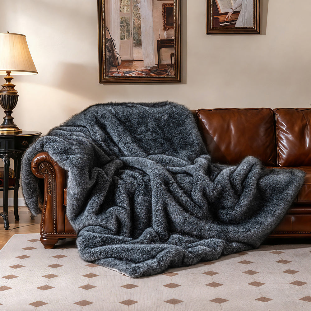 Gray faux wolf fur blanket draped over a brown sofa, featuring a soft plush texture for cozy warmth and comfort.