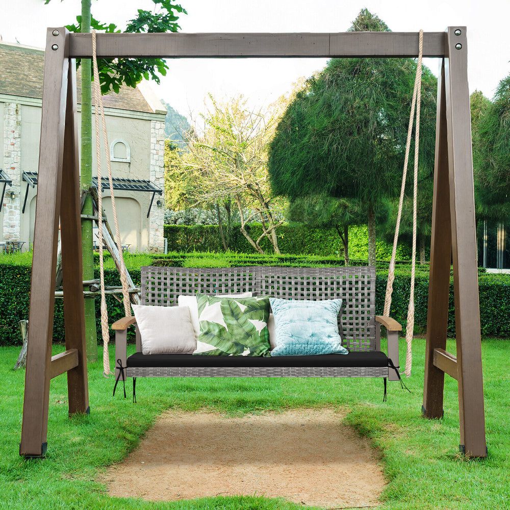 2-person patio wicker hanging swing chair with black cushion, featuring acacia wood armrests for backyard relaxation.