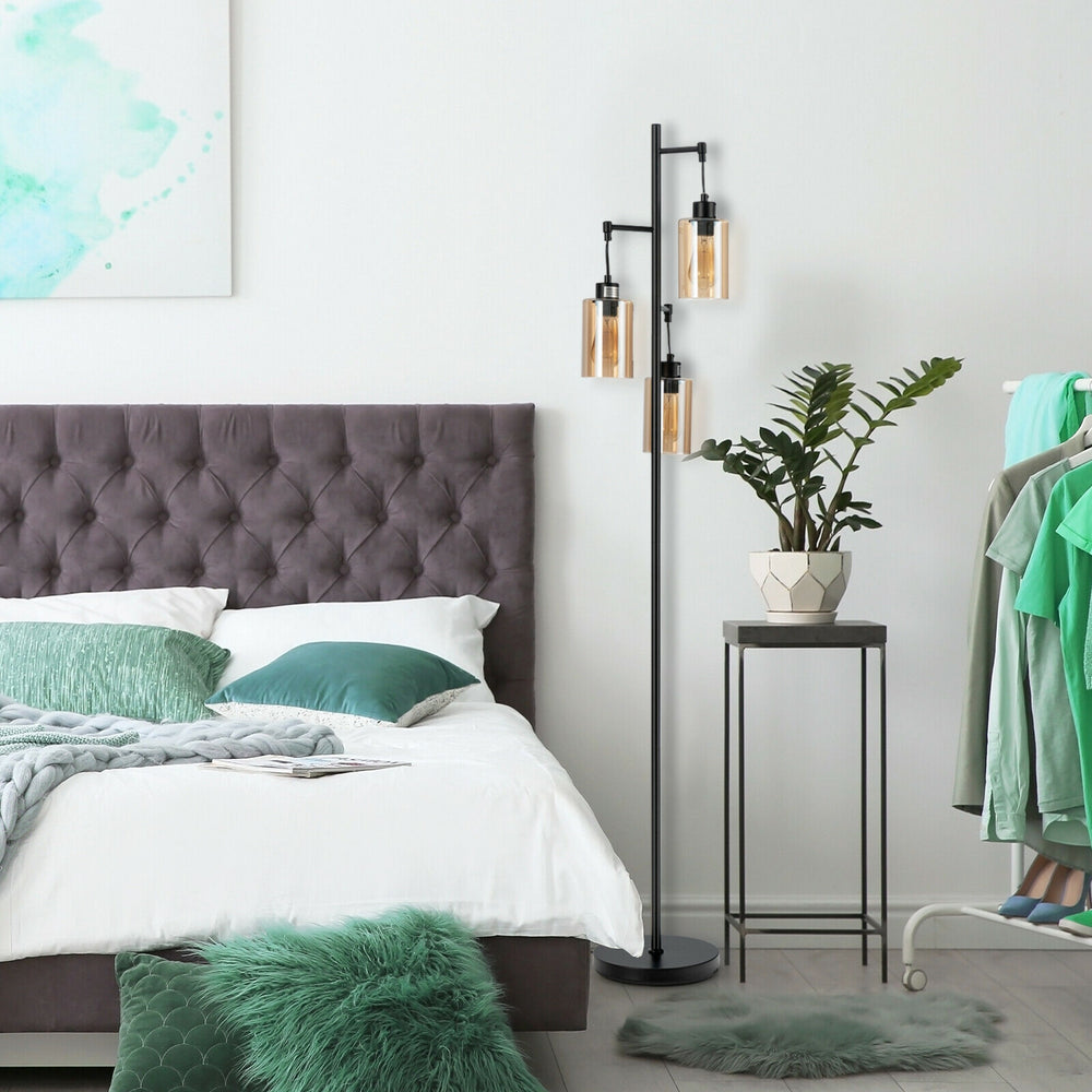 Retro floor lamp with three amber glass shades, placed beside a bed, adding elegant lighting to a cozy bedroom setting.