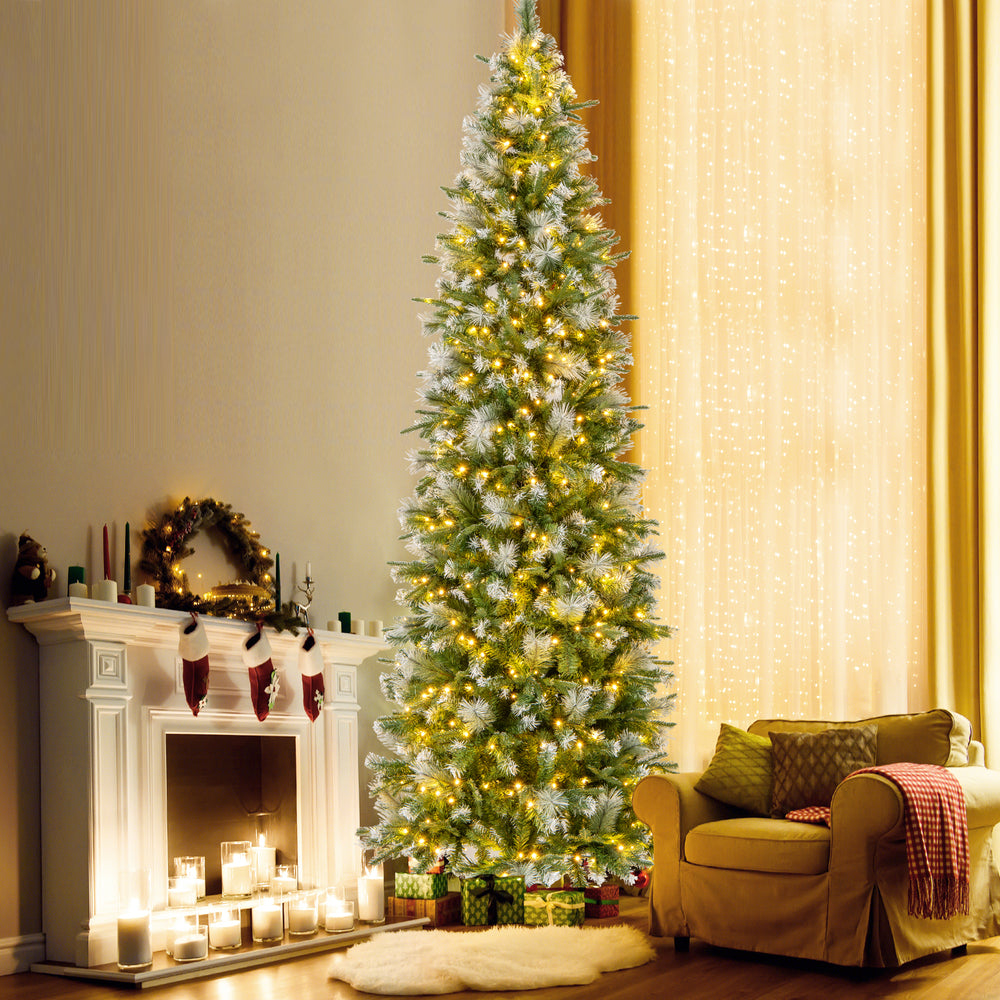 Pencil-shaped 6 FT artificial Christmas tree with warm-white LED lights, providing a cozy glow beside a decorated.