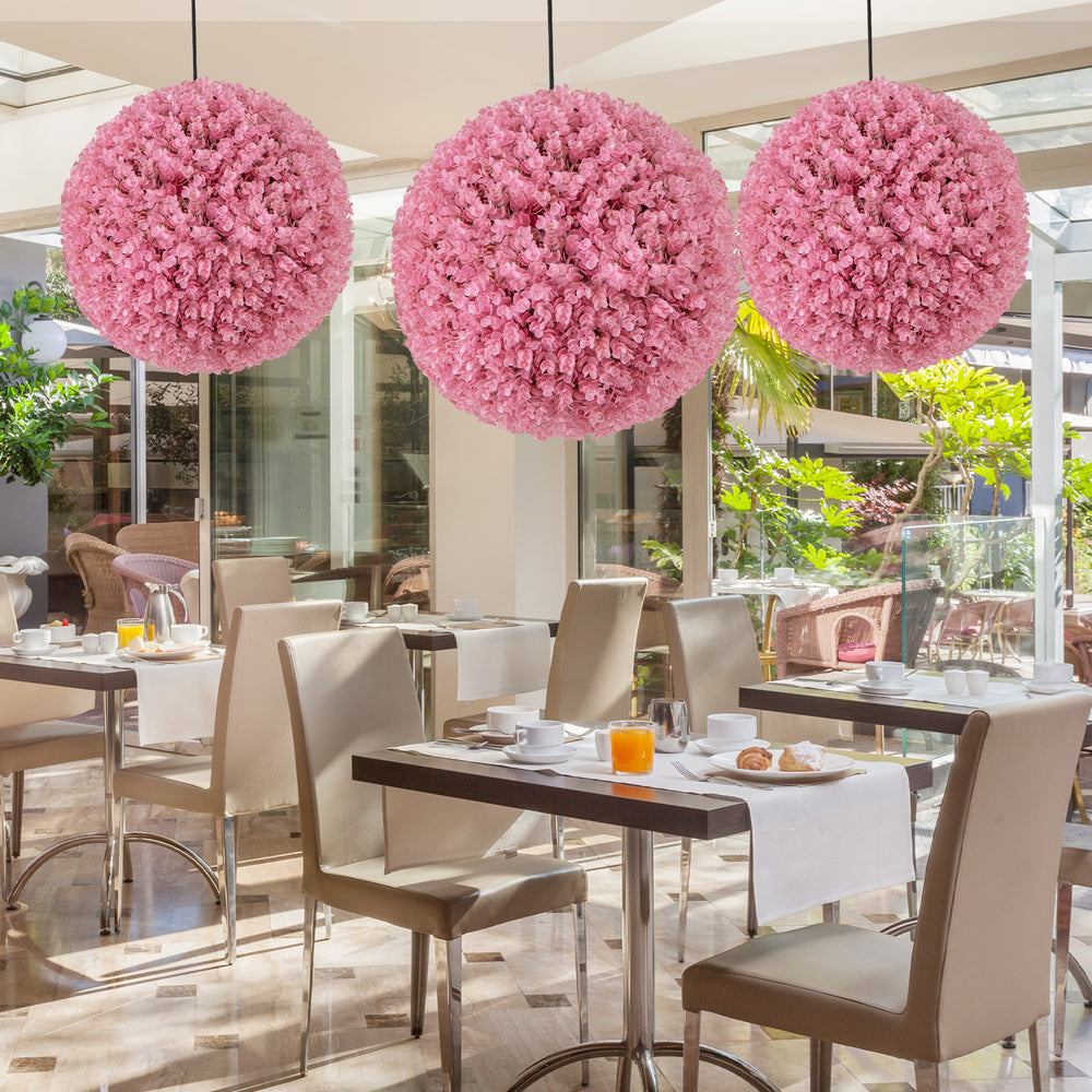 Three 17.5-inch faux pink eucalyptus decorative balls hanging above a dining area, ideal for garden and wedding decor.
