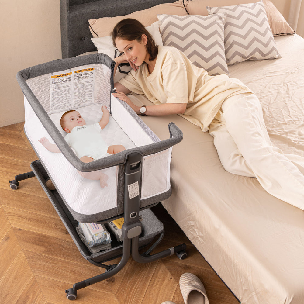 Gray baby bassinet bedside sleeper with clear height adjustment indicators and lockable wheels for safe, versatile use.