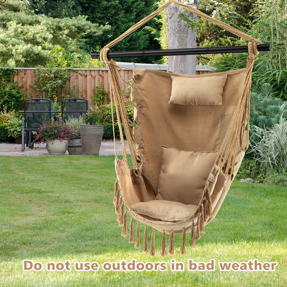 Beige hanging rope swing chair with soft pillow and cushions, featuring elegant tassels, perfect for outdoor relaxation.