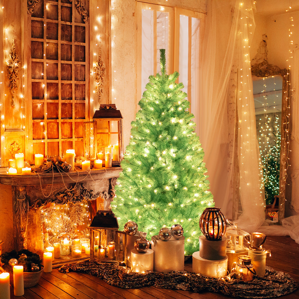 Blue artificial Christmas tree with warm white LED lights, set in a cozy holiday scene with candles and decorations.
