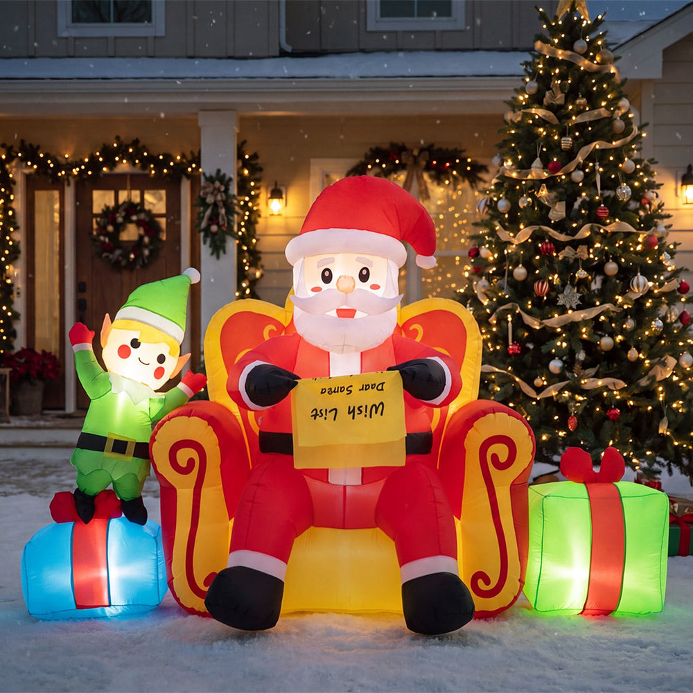 Inflatable Santa Claus on a sofa with an elf and gift boxes, featuring warm white LED lights for festive outdoor display.