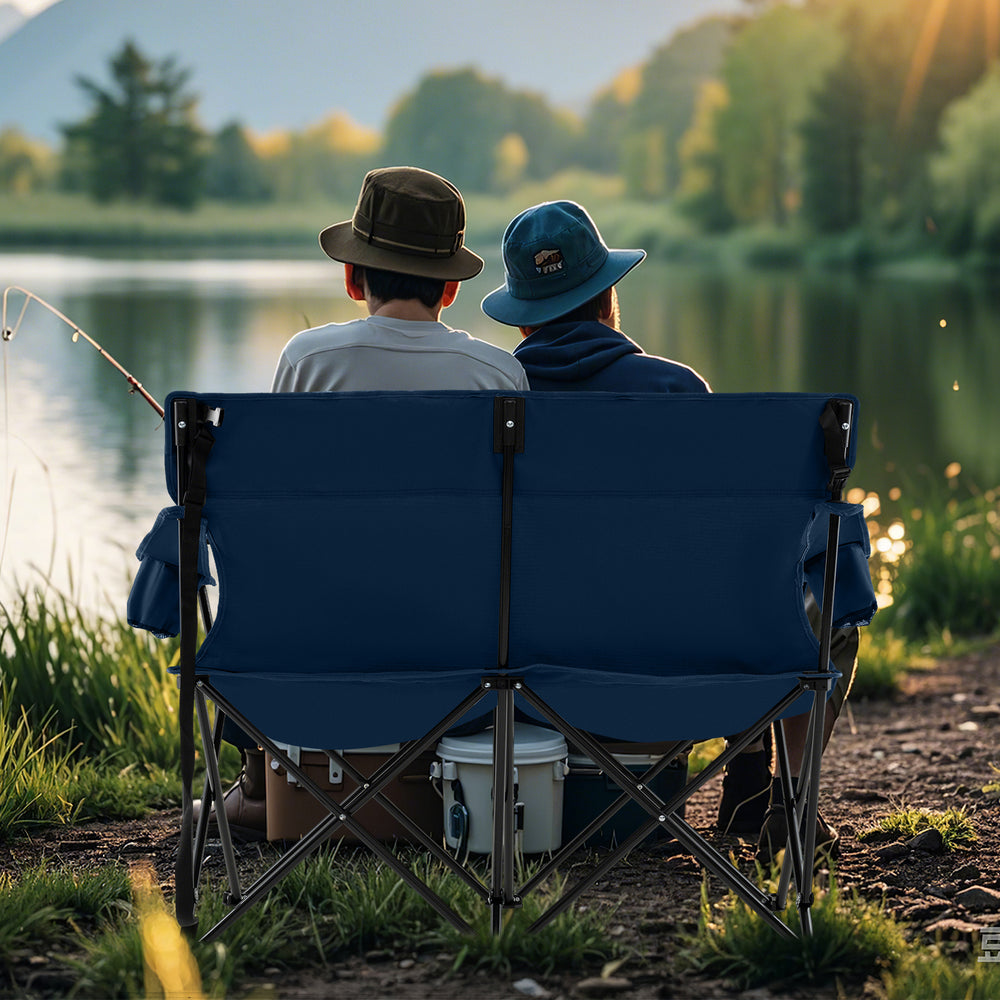 Double camping chair in blue, seating two adults, featuring cup holders, high backrest, and sturdy frame by the lake.