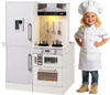 Child chef smiling next to the dual-sided kids play kitchen in white, featuring a pot, frying pan, and luminous range.