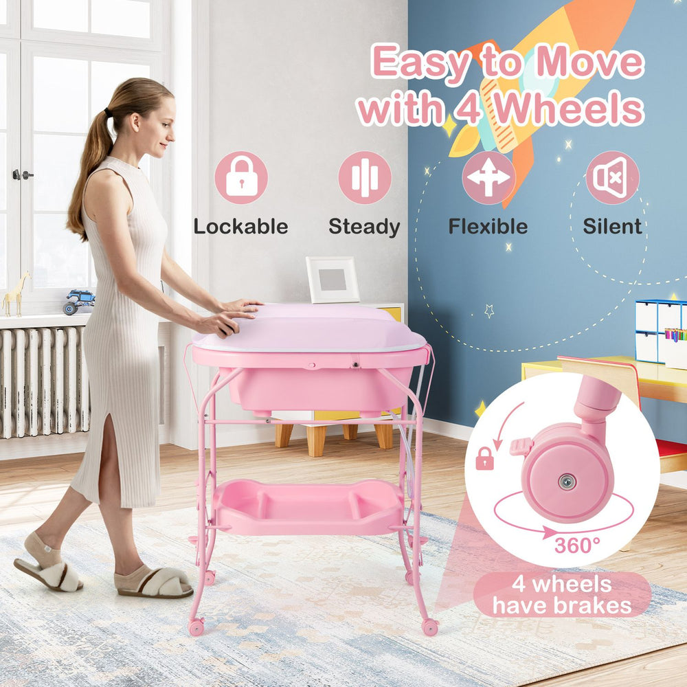Pink foldable diaper changing table on wheels shown beside a parent, with bathtub and storage shelf for babies and infants.